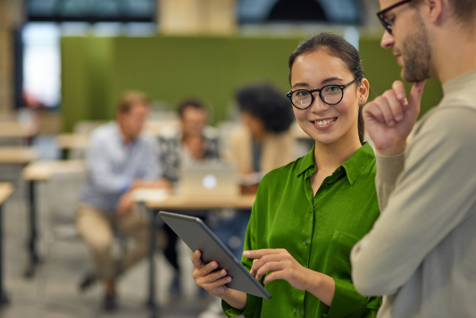 Woman using a tablet with glasses, talking to a colleague